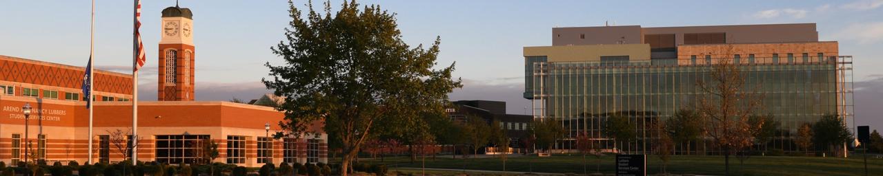 Sunset lighting a wide view of campus including the clock tower, library, and Student Services Building